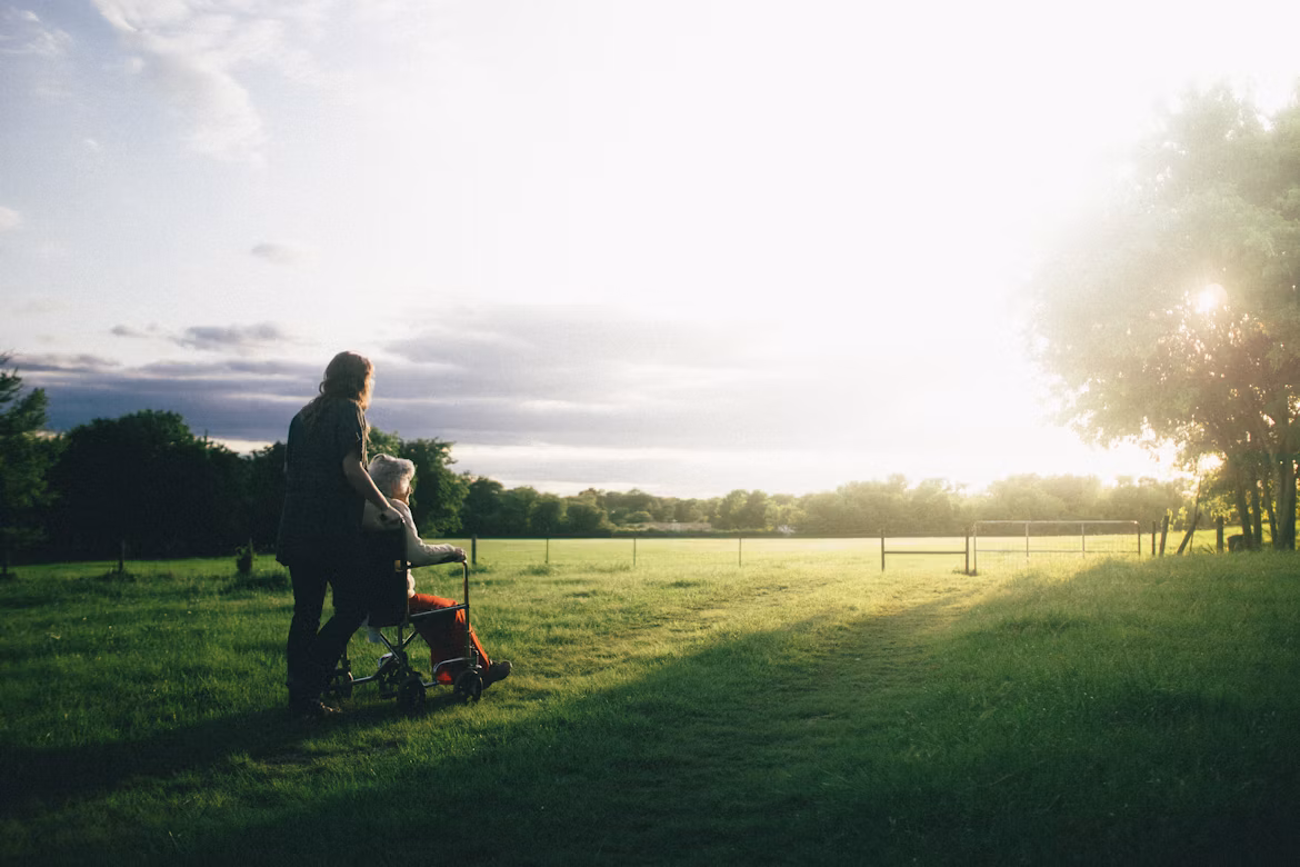 Caregiver walking beside a client through a peaceful field at sunset